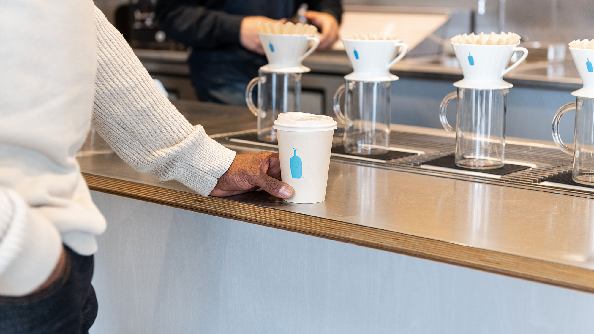 A young guy holding a white and blue coffee cup in a cafe