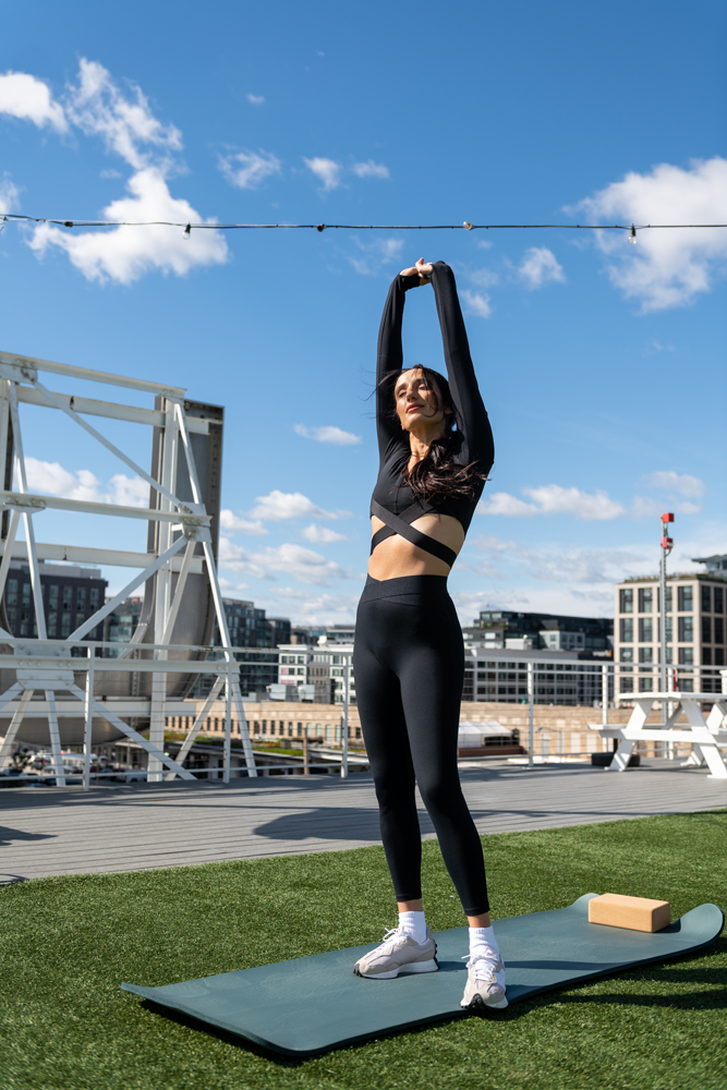 A woman practicing yoga on a roof top deck under a sunny blue sky