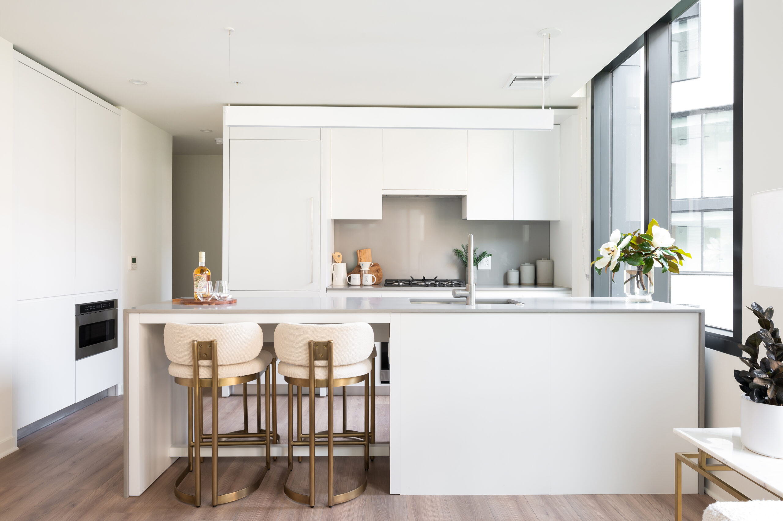 Margarite luxury apartments' kitchen in Washington, DC, with white cabinets, countertop, & gold stools.